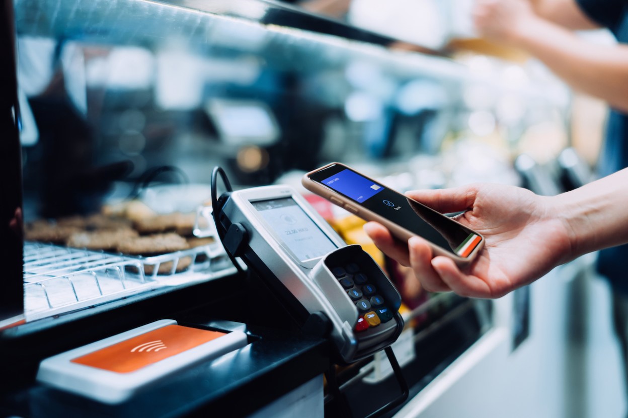 Close up of a woman's hand paying with her smartphone in a cafe, scan and pay a bill on a card machine making a quick and easy contactless payment. NFC technology, tap and go concept.