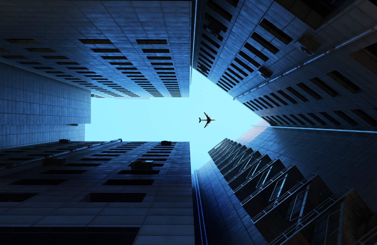 Digital generated image of buildings making arrow sign with airplane flying on blue sky.