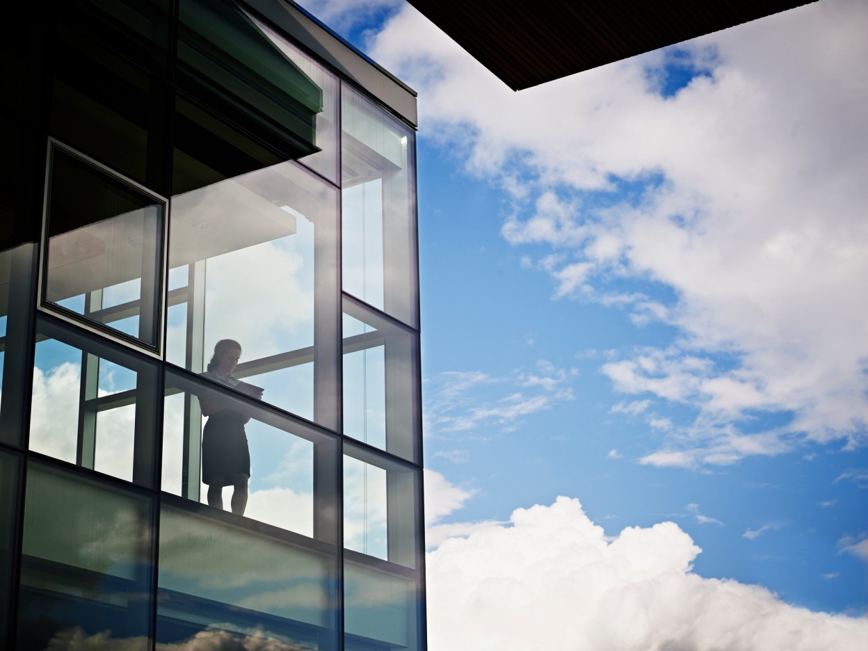 silhouette of an executive looking out at a cloudy sky in a glassy corner office